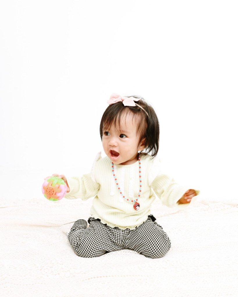 Baby with a pink bow playing with a toy ball, first birthday photoshoot at The Cade & Co studio Cyberjaya