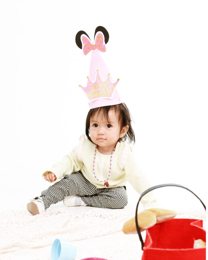Baby sitting in a party hat on a white backdrop, first birthday photoshoot at The Cade & Co studio Cyberjaya