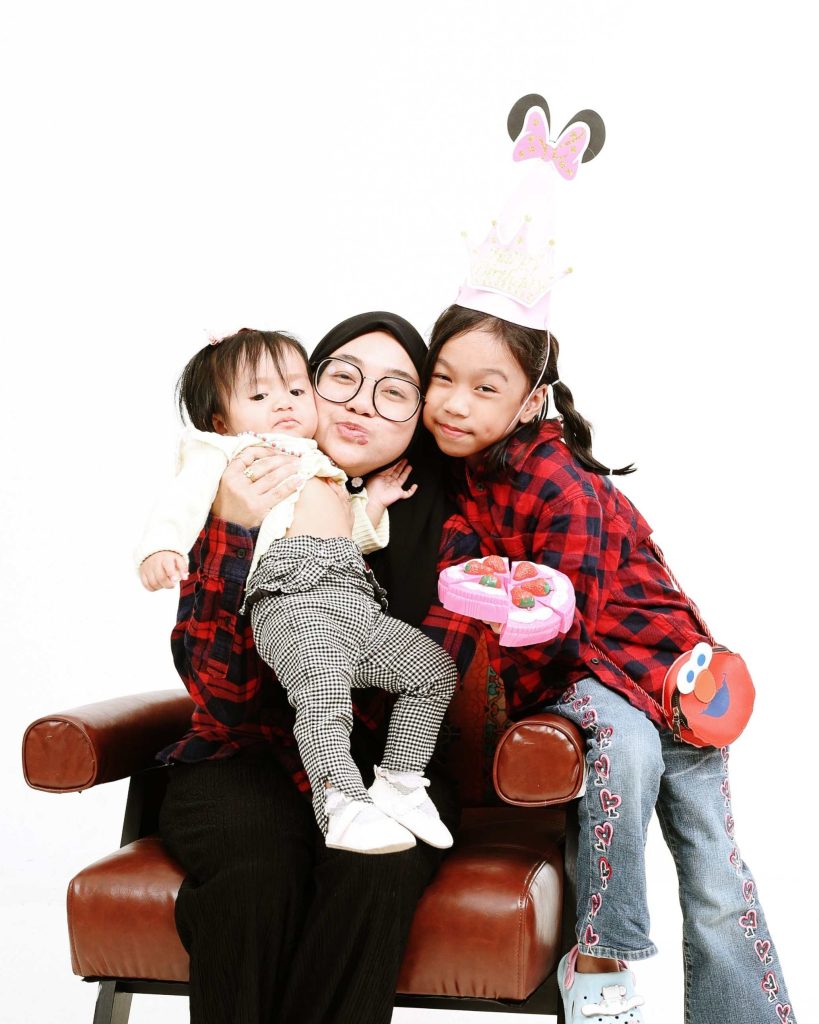 Mother kissing her daughters on a sofa, first birthday photoshoot at The Cade & Co studio Cyberjaya