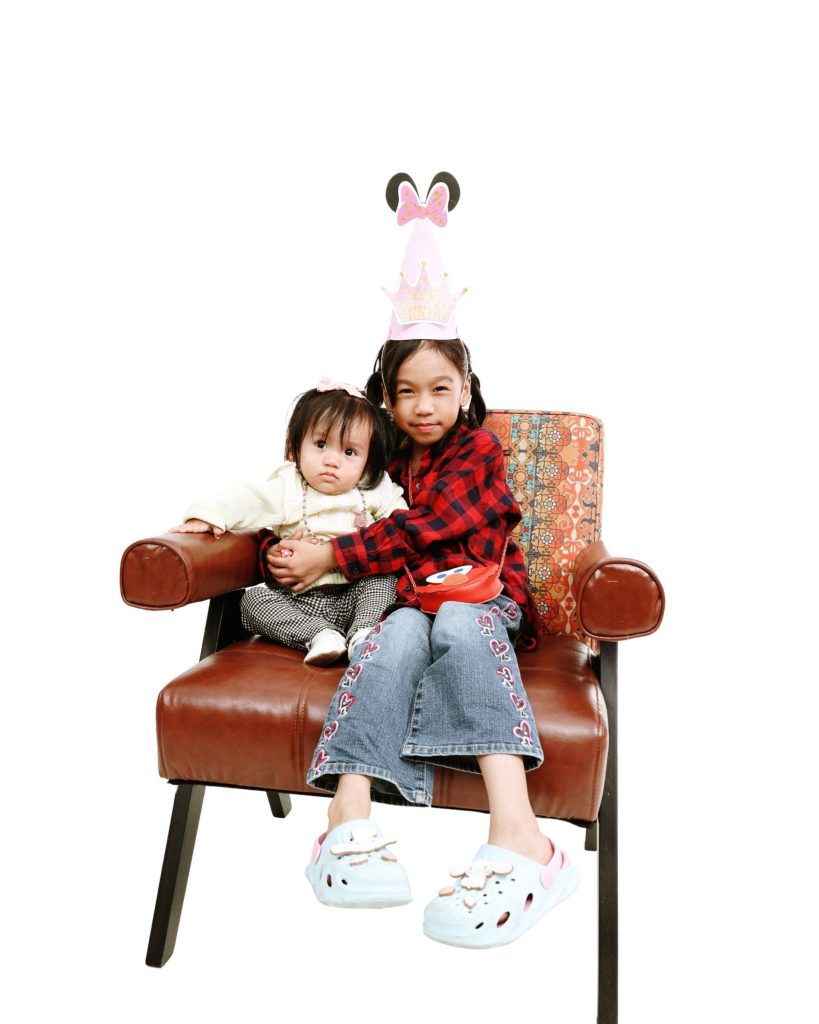 Sisters on a vintage armchair, first birthday photoshoot at The Cade & Co studio Cyberjaya