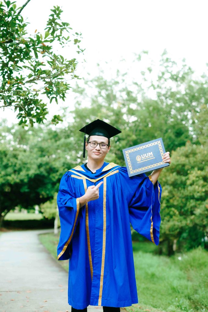 Tan Kim giving a thumbs-up with his UUM scroll, outdoor graduation photoshoot